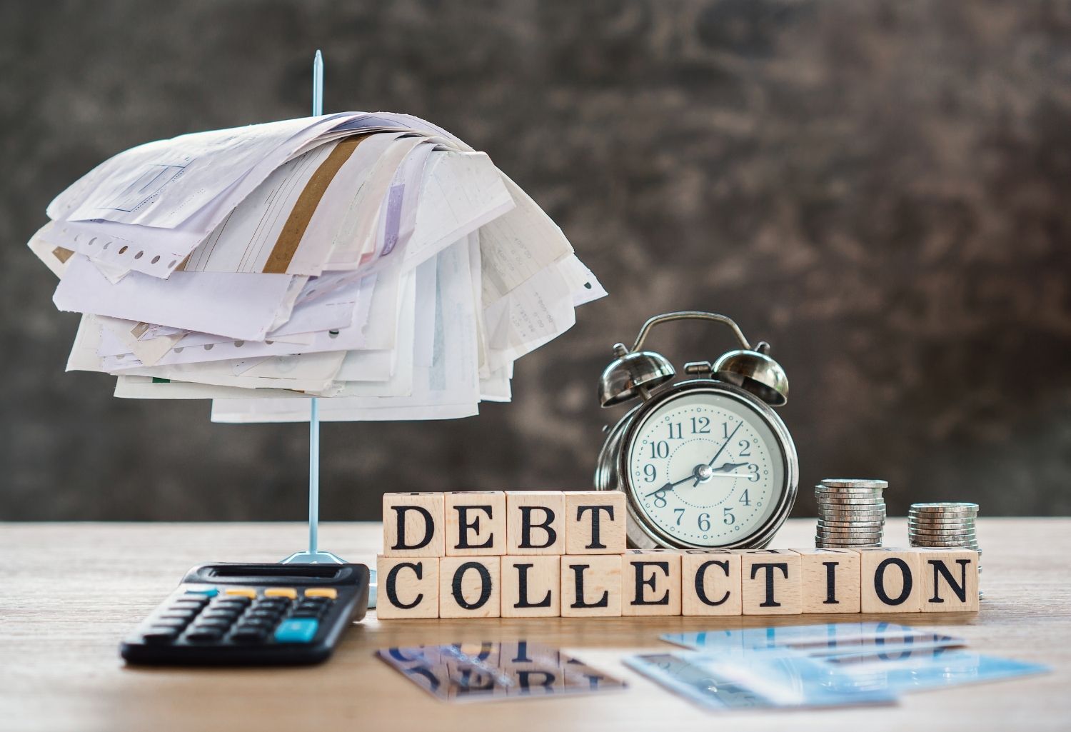 The words debt collection on a desk with money a clock, a calculator, incoives, credit cards and more. This image represents Commercial Debt Collection.